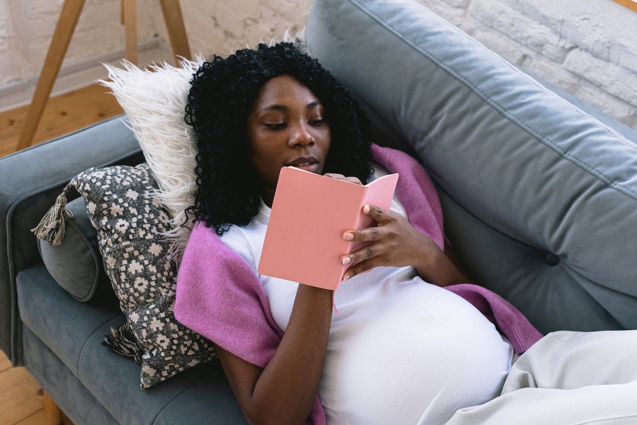 11 weird pregnancy symptoms. Pictured: a pregnant woman lying on a couch and writing in a pink notebook.