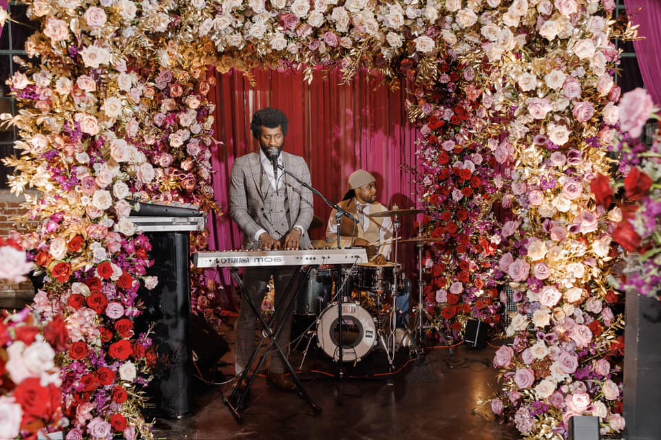 A wedding floral arrangement surrounding a stage where a man is singing and playing the piano