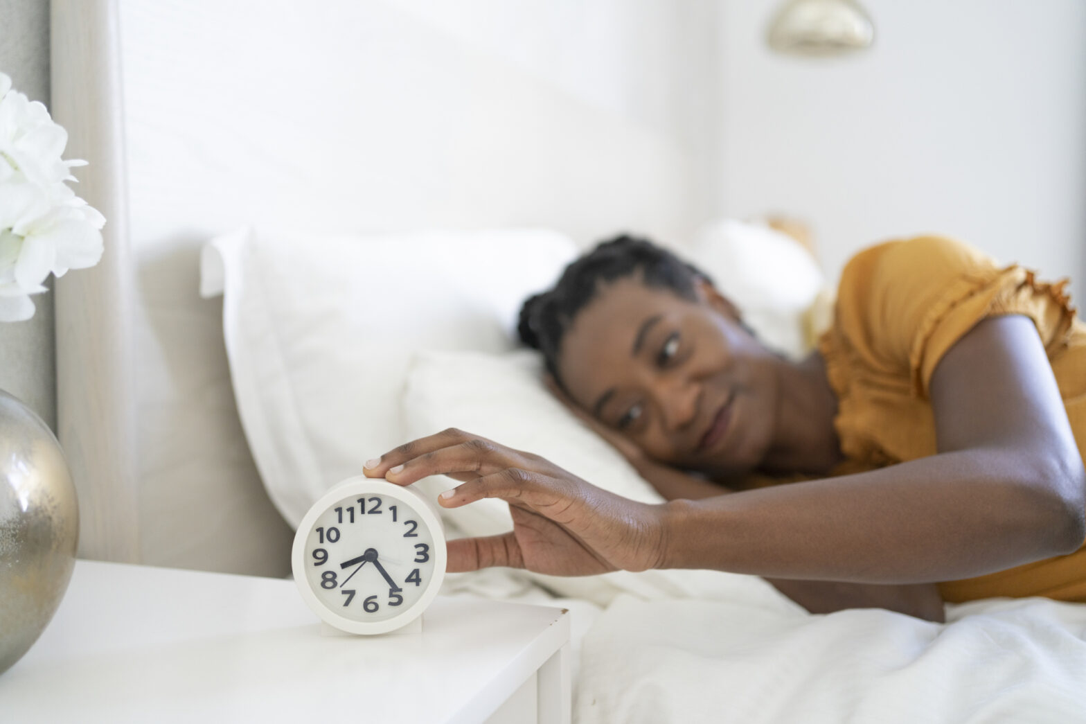 Smiling woman turning off alarm clock lying on bed at home