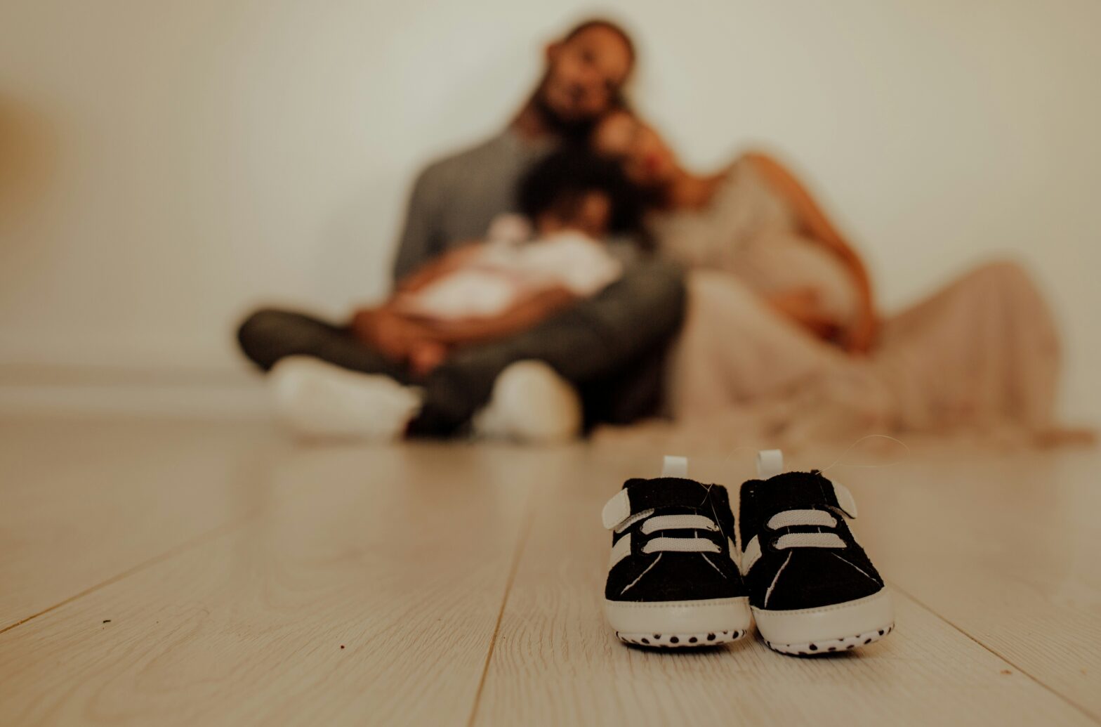 Picture of Black family in background with pair of baby shoes in the front