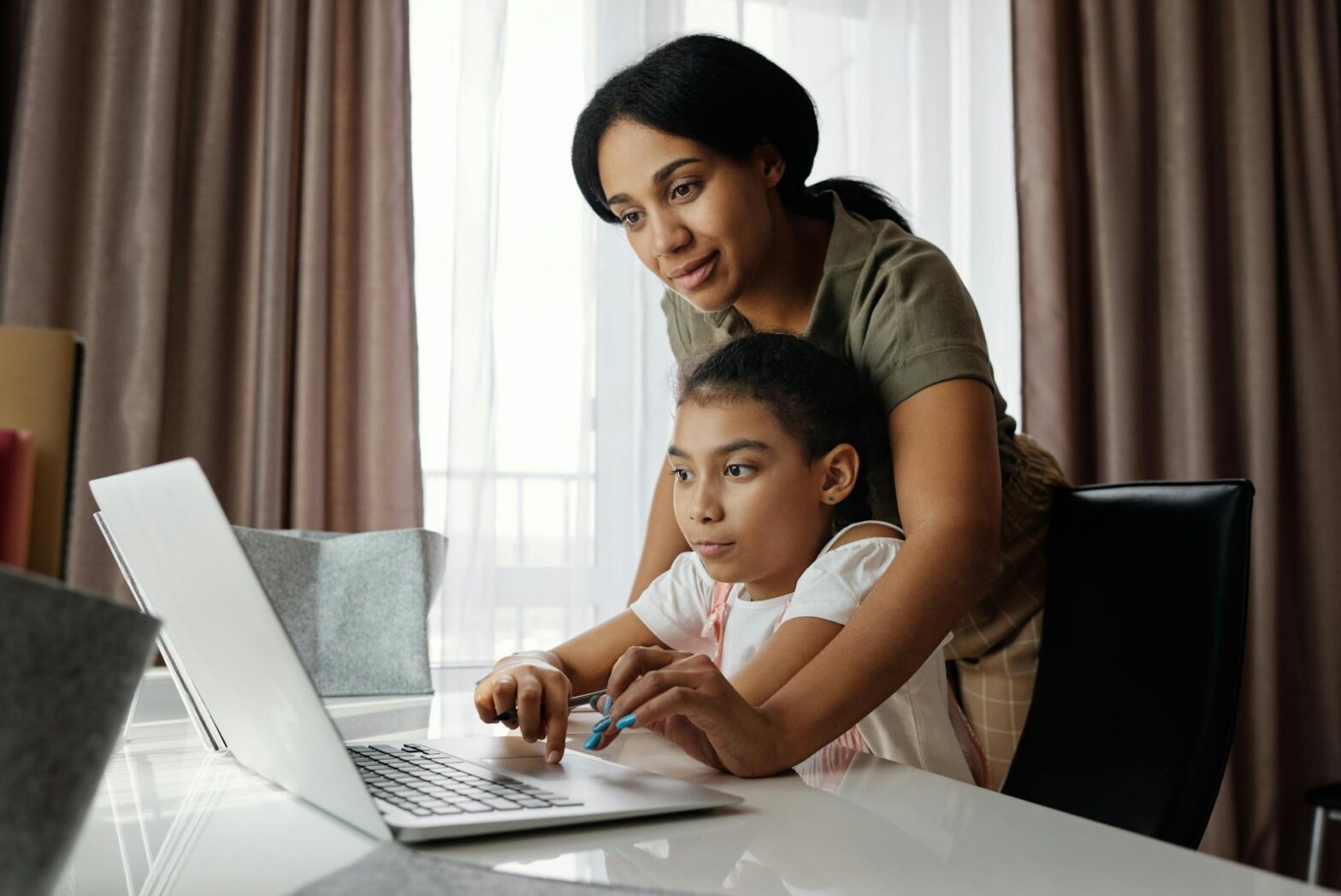 A mother helping her daughter use a laptop