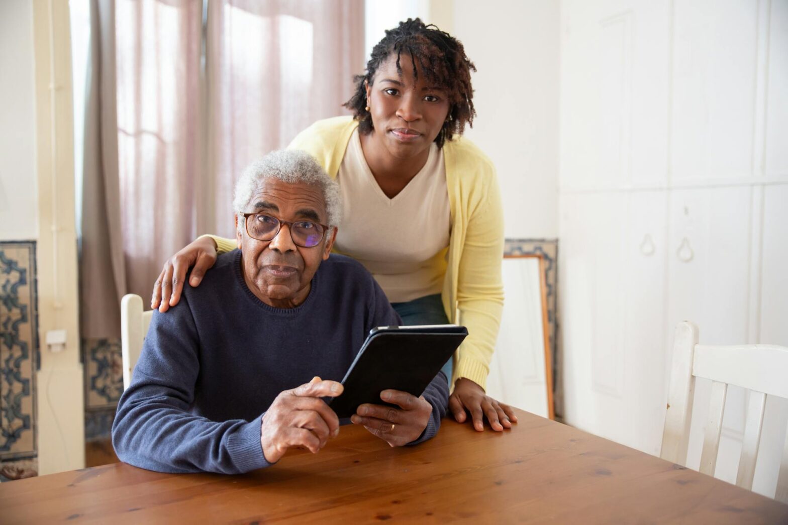 A woman standing beside the elderly man holding a-tablet