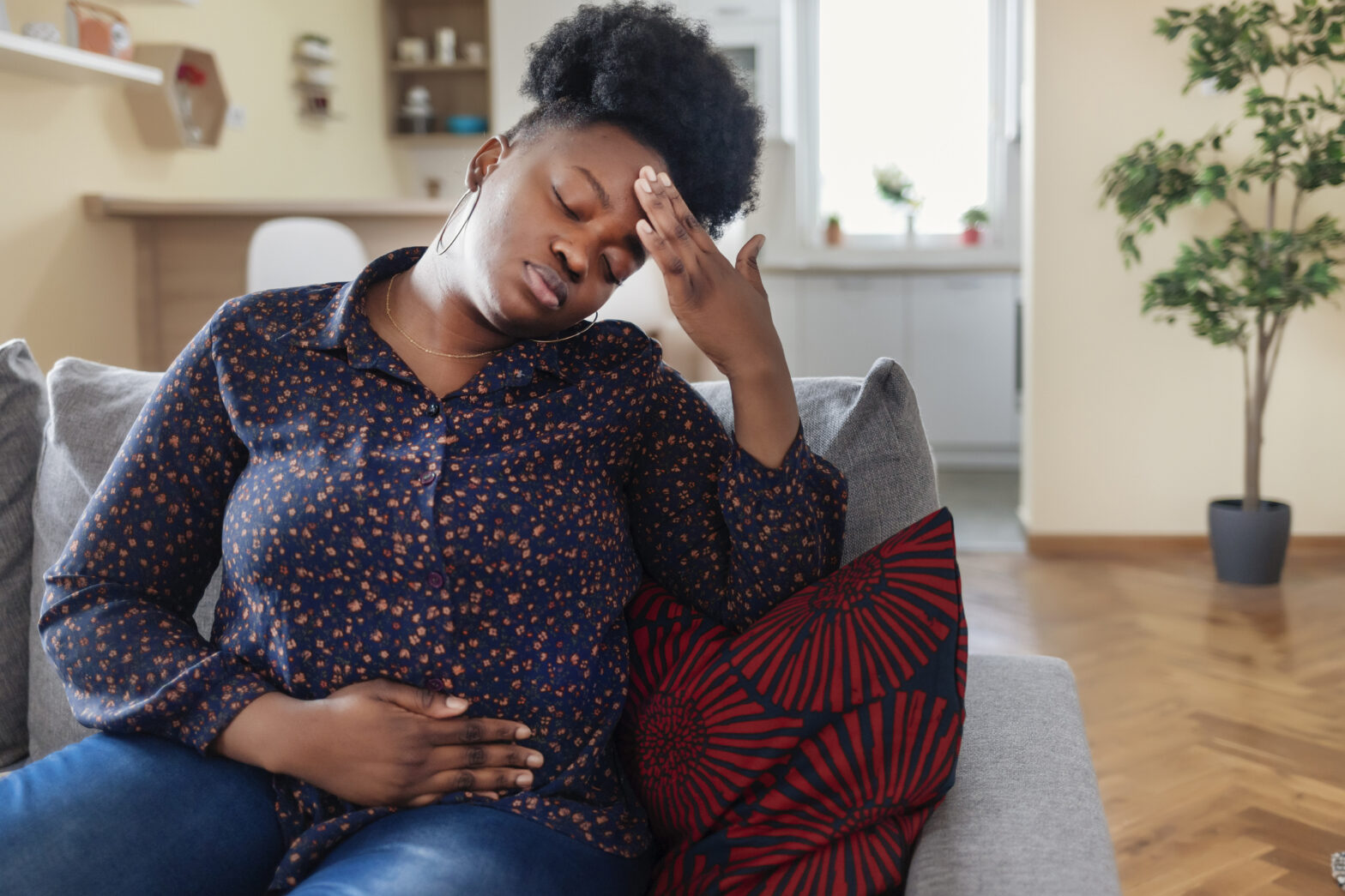 African American Woman Suffering From Strong Abdominal Pain While Sitting on Sofa at Home