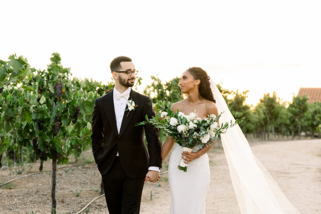 A couple walking in a vineyard while the bride hold a bouquet