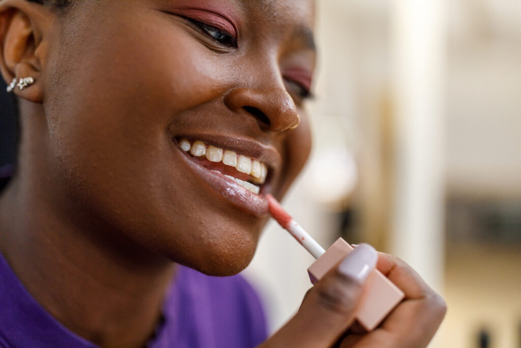 African woman using lip gloss in front of the mirror