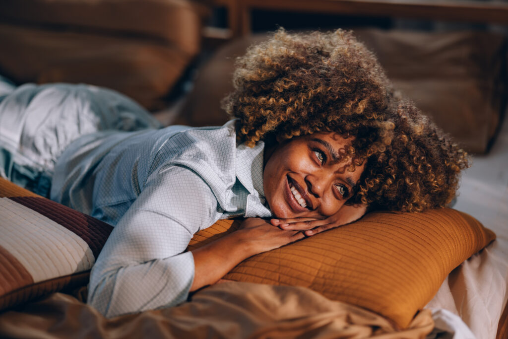 A smiling African-American female lying on the cozy bed and enjoying tranquil morning at the weekend.