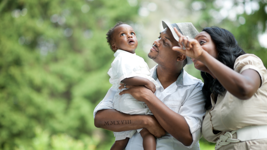 Roman Numeral Family tattoo on the arm of a father holding a baby with a woman nearby