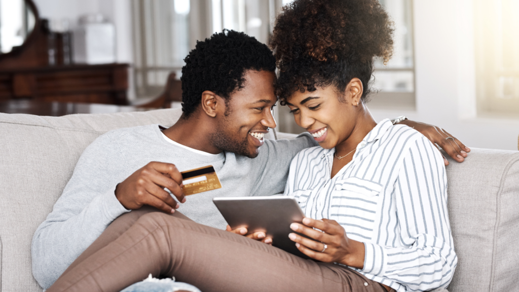 Black couple smiling on couch holding credit card and tablet