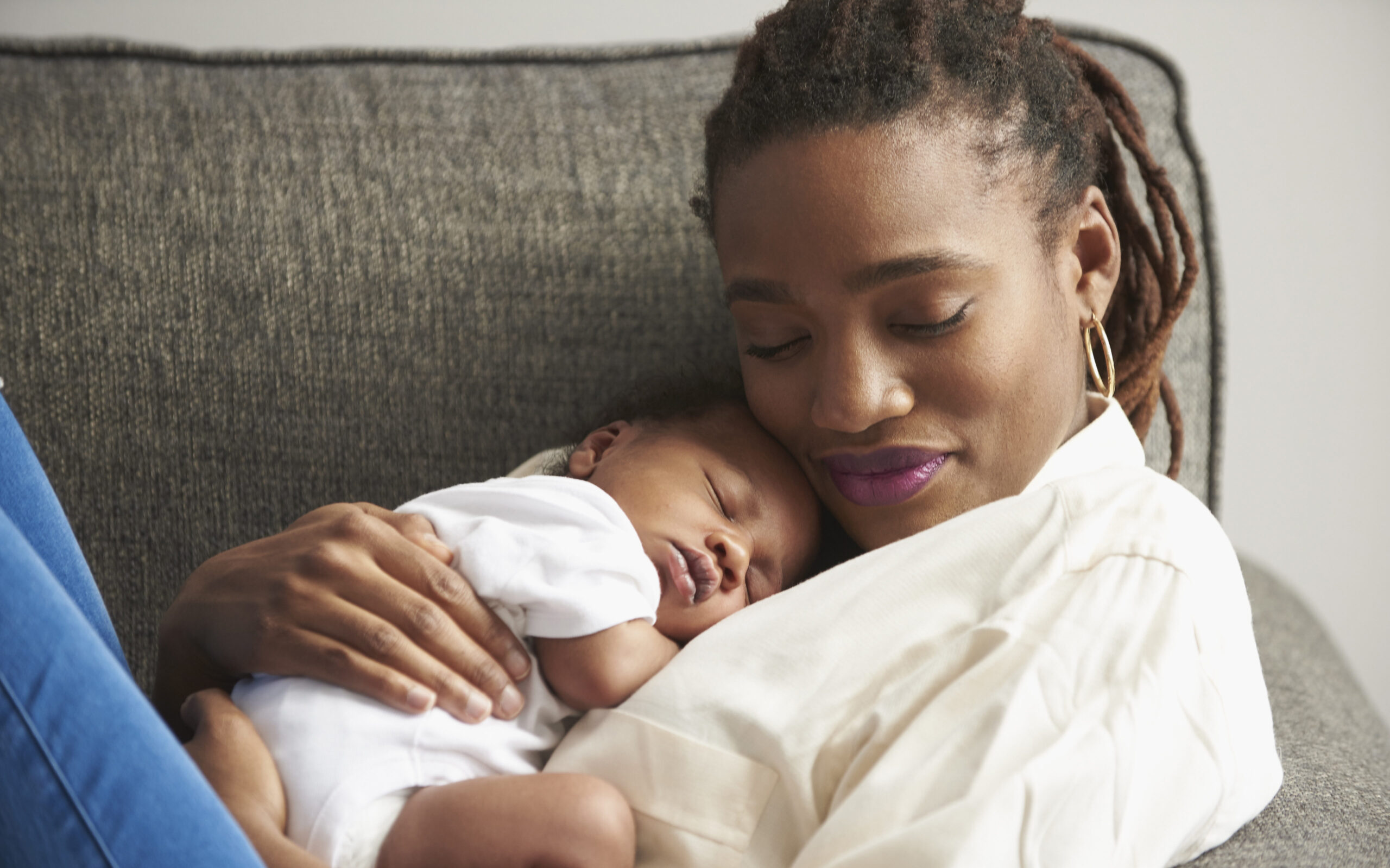 Black mother cuddling sleeping baby son on sofa; safe sleep practices