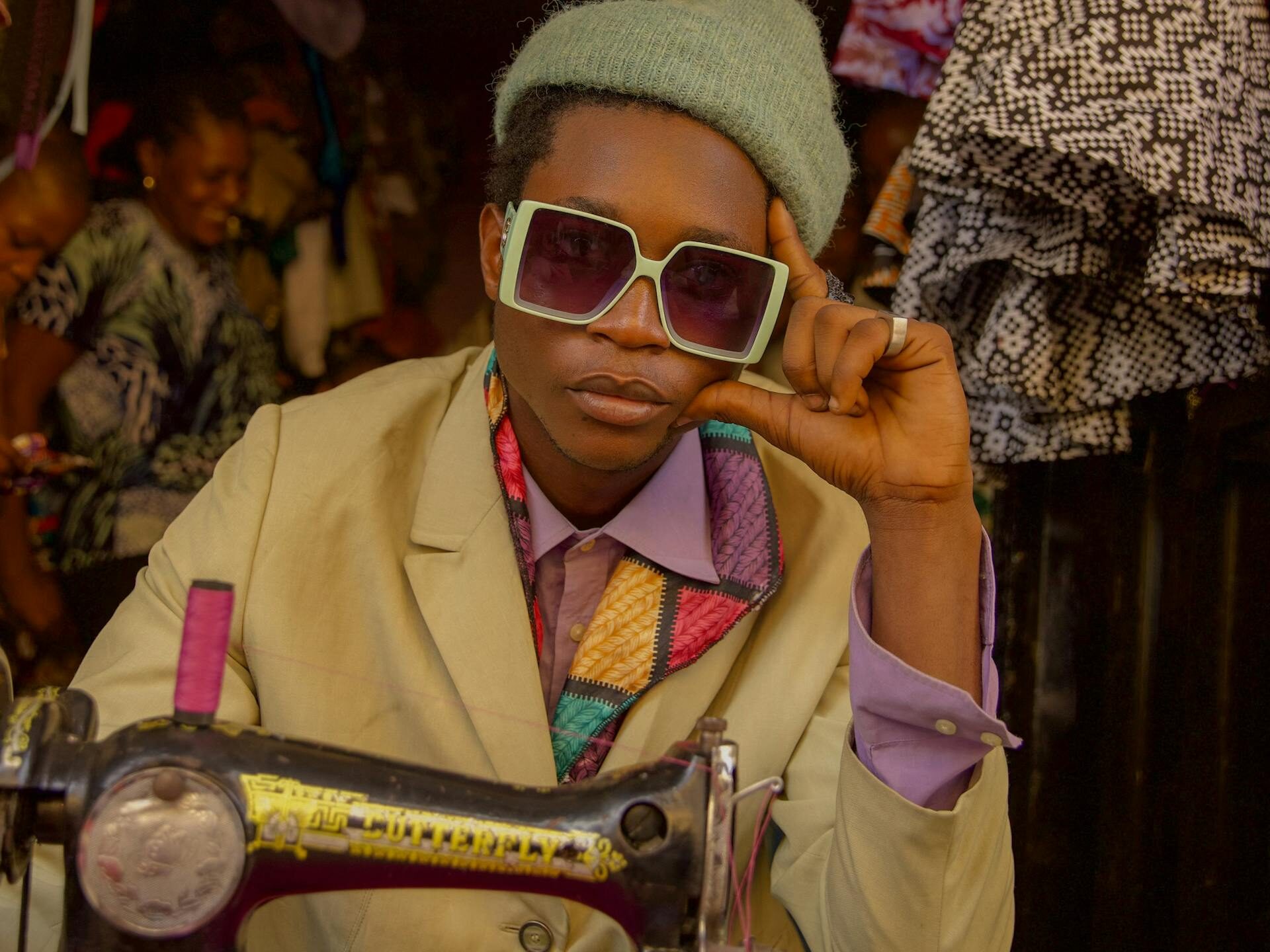 Black man wearing shades looks bored while sitting in front of sewing machine and cloth material