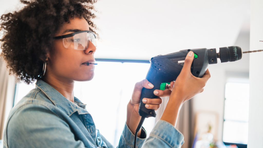 Afro woman drilling wall with electric drill