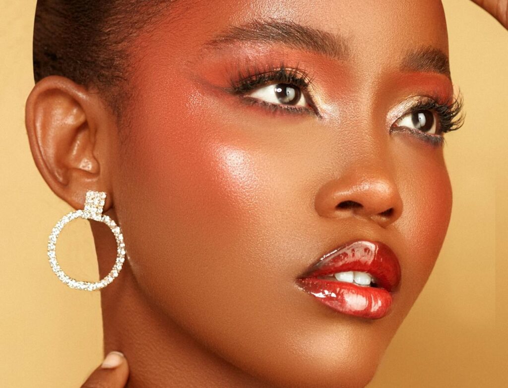 Brown-skinned woman wearing foundation with rosy cheeks and medium-red lipstick and eyeshadow