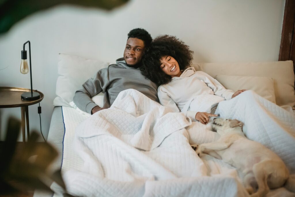 Couple snuggles in bed with a dog on the top of the blanket