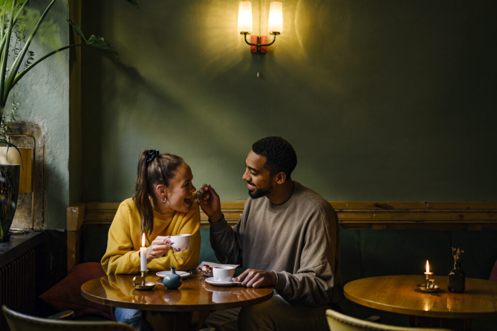 Wide shot of boyfriend feeding girlfriend a bite of dessert