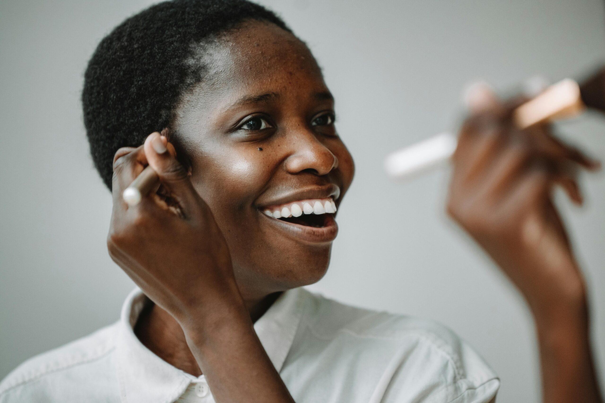 Black woman with short hair applying makeup to deep toned skin