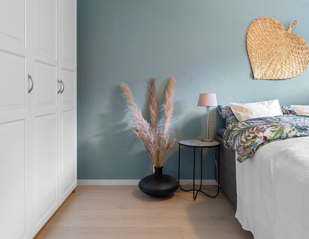 Blue wall, large fan on wall and bedroom drawers