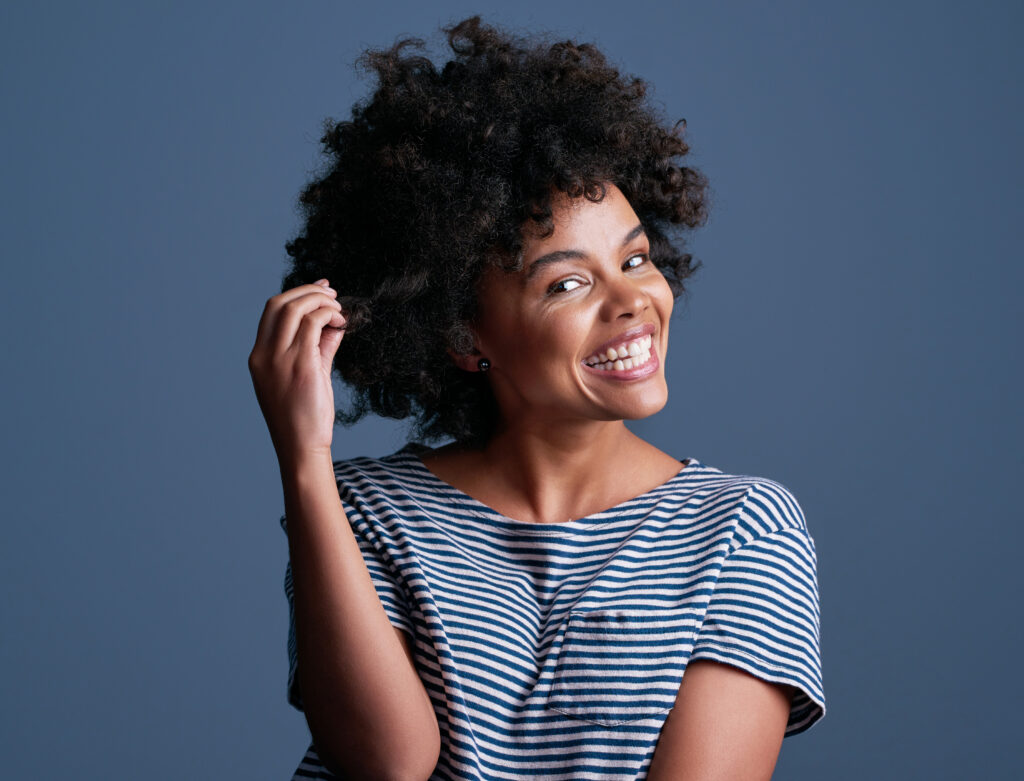 Studio shot of an attractive young woman playing with her hair against a blue background 	