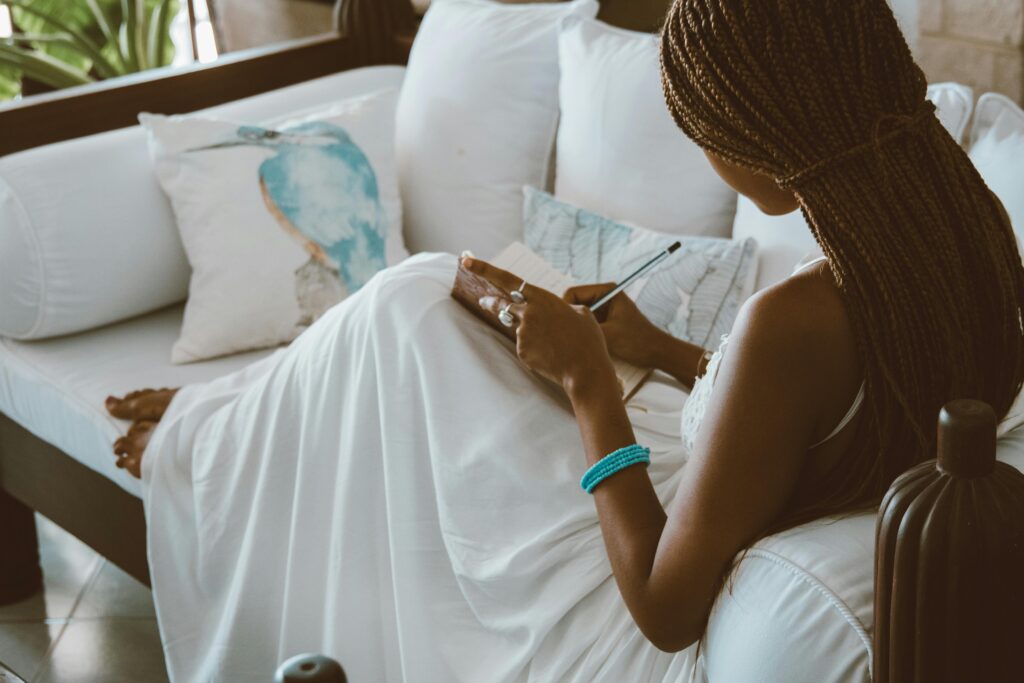 Black woman sitting on the couch writing in a journal. junk-journaling