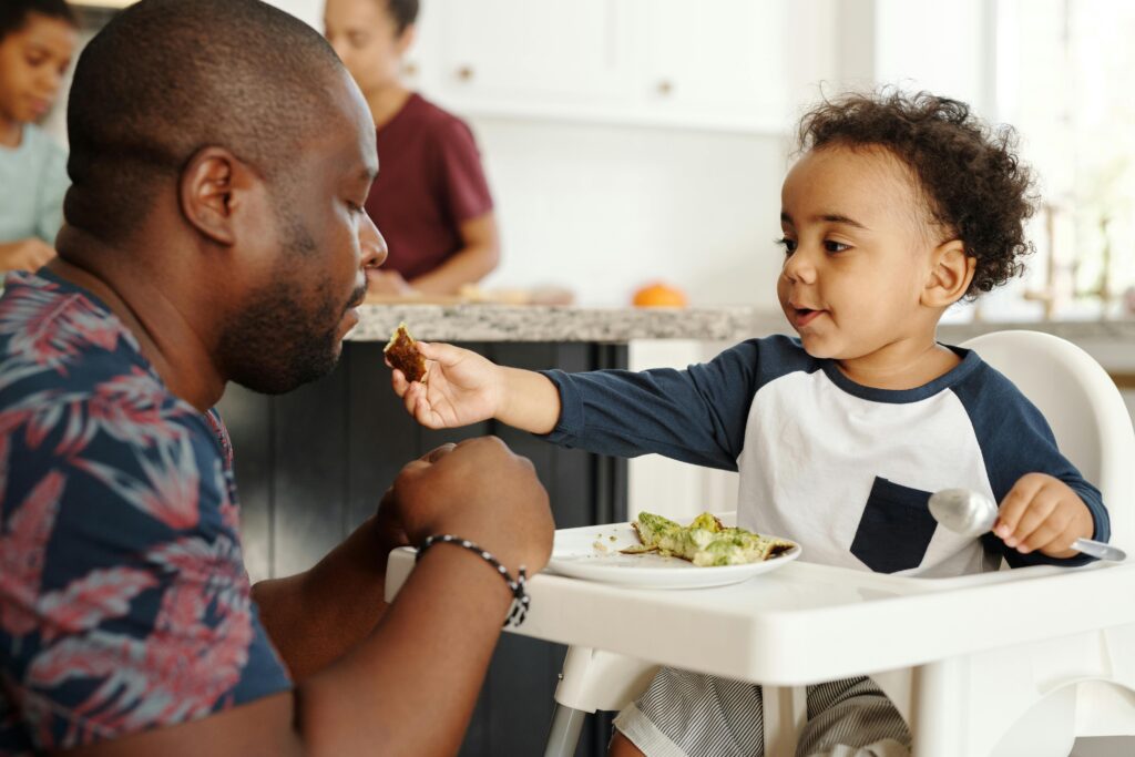 1 Year Old Lunch Father and child sharing lunch while toddler sits in a high chair